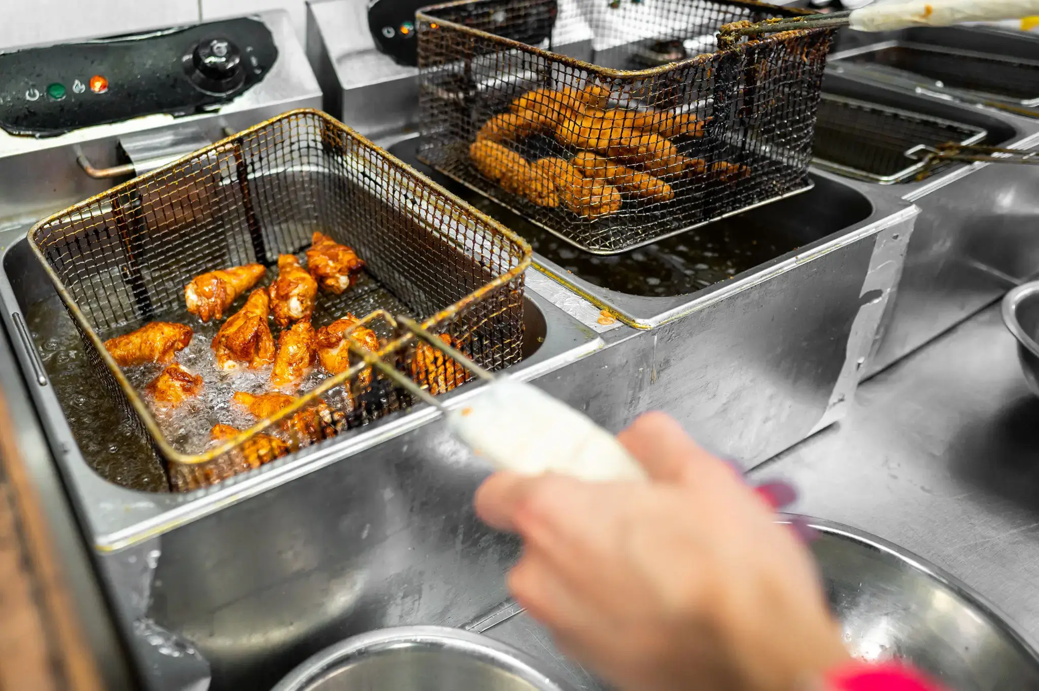 Fried chicken pieces and skewers cooking in deep fry baskets at a food stall.
