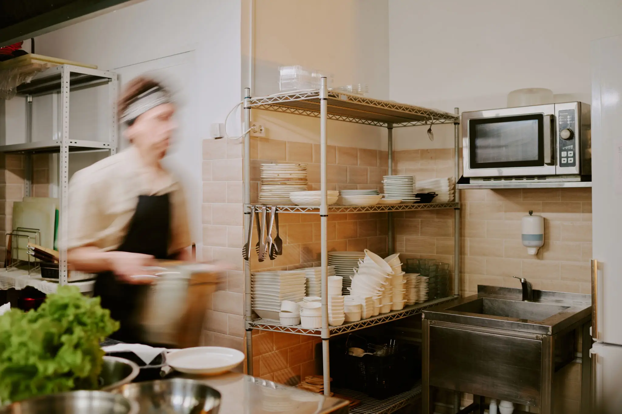 Blurred person cooking in a kitchen with shelves of containers.