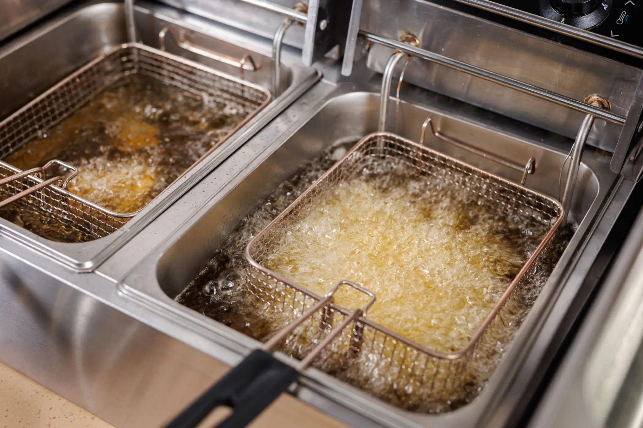 Two baskets frying food in hot oil in a commercial deep fryer.