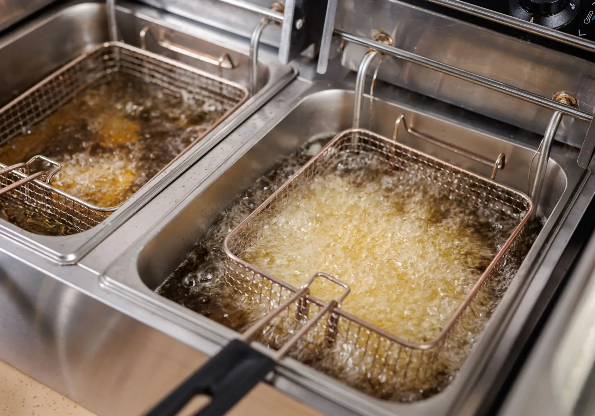 Two baskets frying food in hot oil in a commercial deep fryer.
